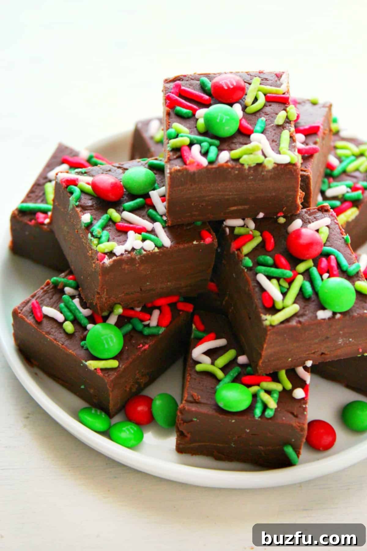 Christmas Fudge Recipe: Easy 3-Ingredient Treat Rich, creamy chocolate fudge squares adorned with festive sprinkles on a white plate, ready for holiday enjoyment.