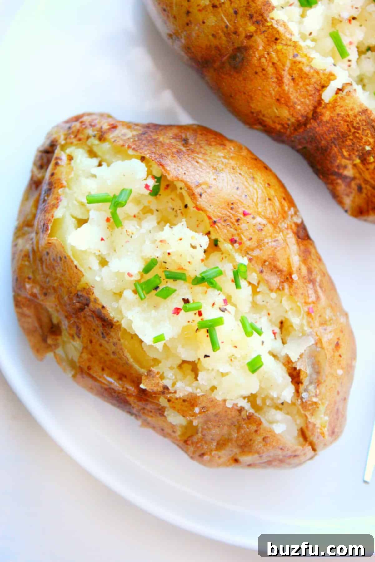 A perfectly cooked microwave baked potato, sliced open and ready for toppings, on a white plate.