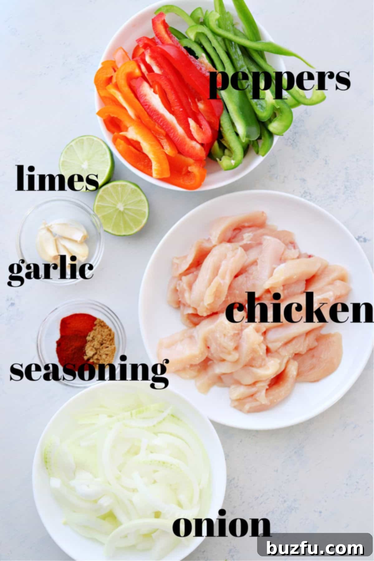 Chicken fajitas ingredients Ingredients for fajitas laid out on a white cutting board, including chicken, bell peppers, onion, garlic, and spices.