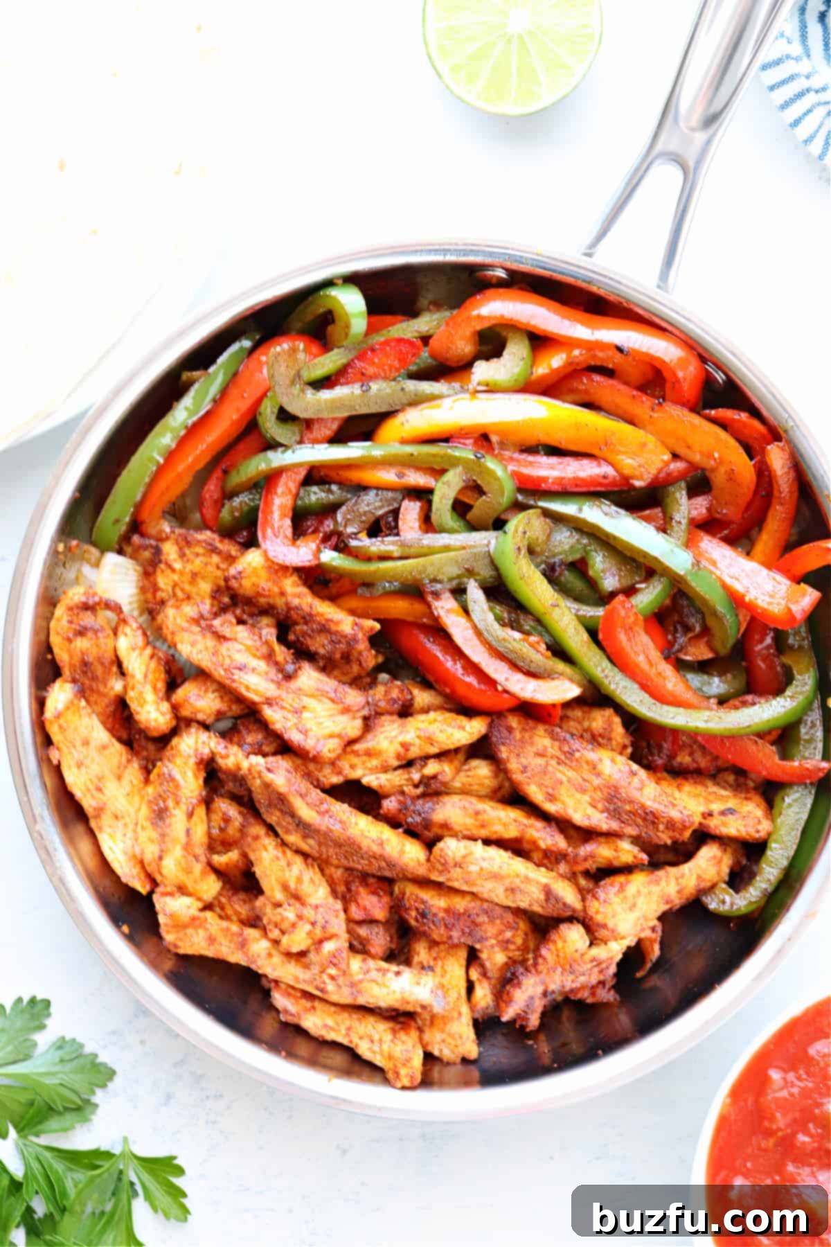 Skillet Chicken Fajitas recipe Skillet with cooked chicken and bell peppers and onions, on a marble cutting board, ready to be served.