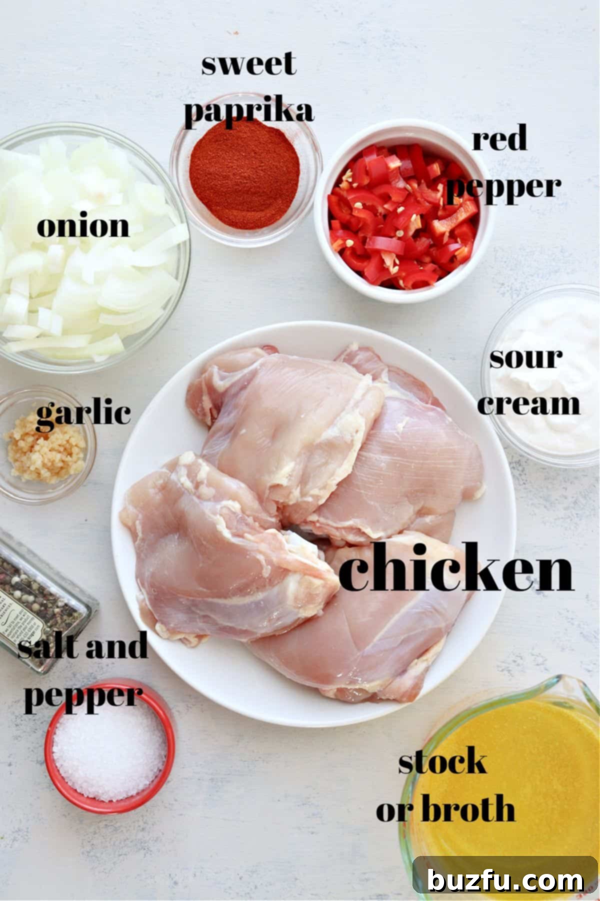 Fresh ingredients laid out for making chicken paprikash: bone-in chicken thighs, red bell pepper, onions, garlic, sweet Hungarian paprika, chicken stock, cornstarch, and sour cream.
