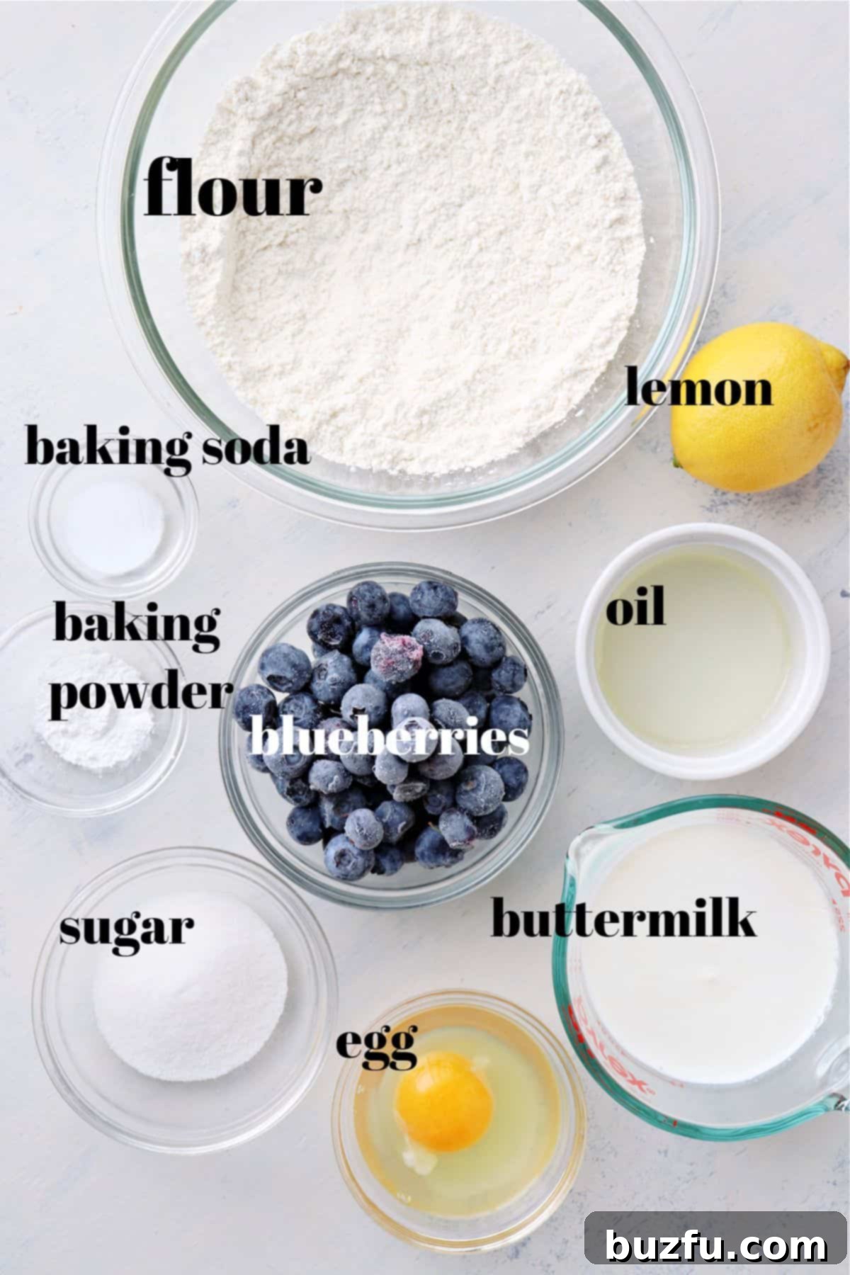 Blueberry pancakes ingredients. Assortment of pancake ingredients including flour, sugar, eggs, buttermilk, and fresh blueberries laid out on a wooden board.