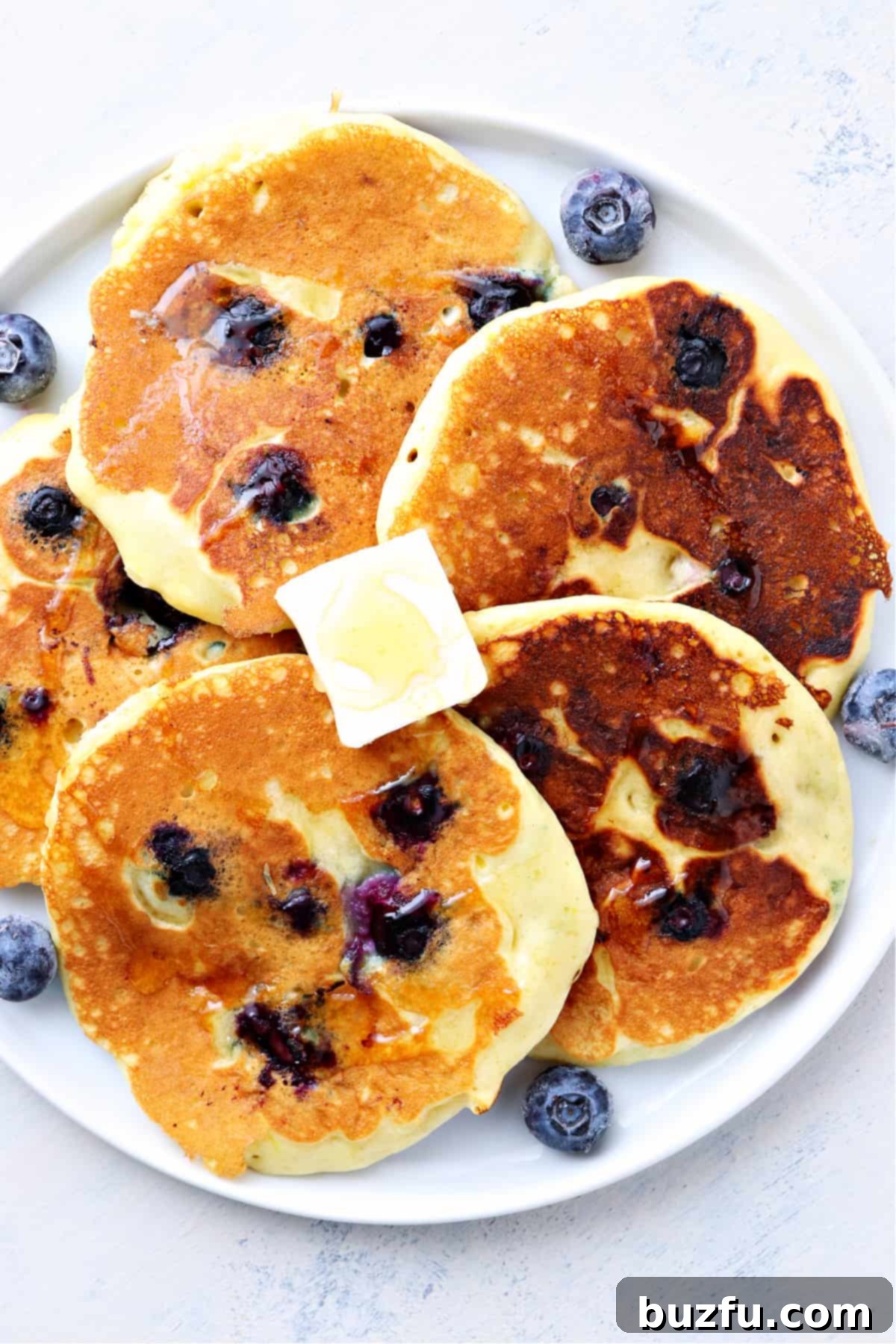 Fluffy blueberry pancakes. Five fluffy golden blueberry pancakes stacked on a white plate, drizzled with honey and garnished with fresh blueberries.