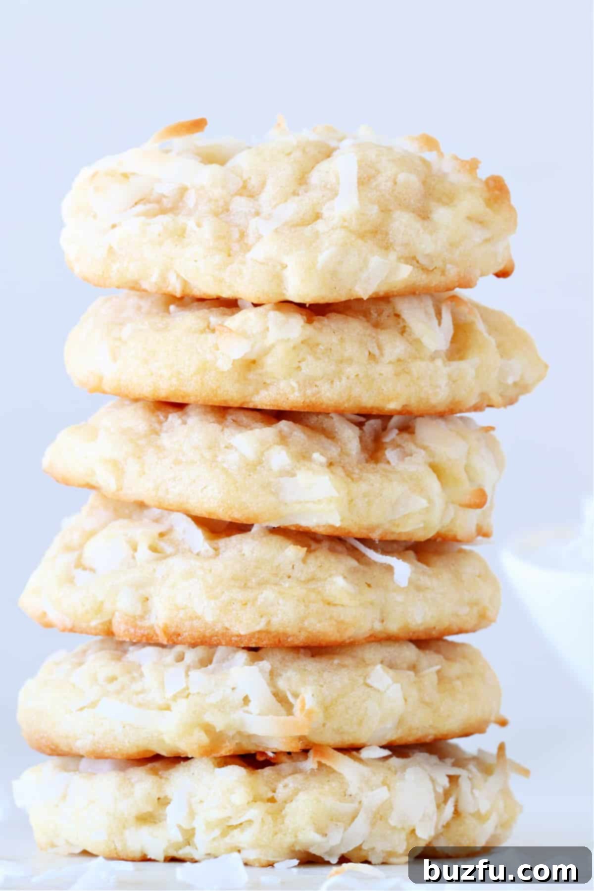 Best Homemade Coconut Cookies Recipe Freshly baked Coconut Cookies stacked on a white plate, showcasing their thick, chewy texture and golden-brown edges.