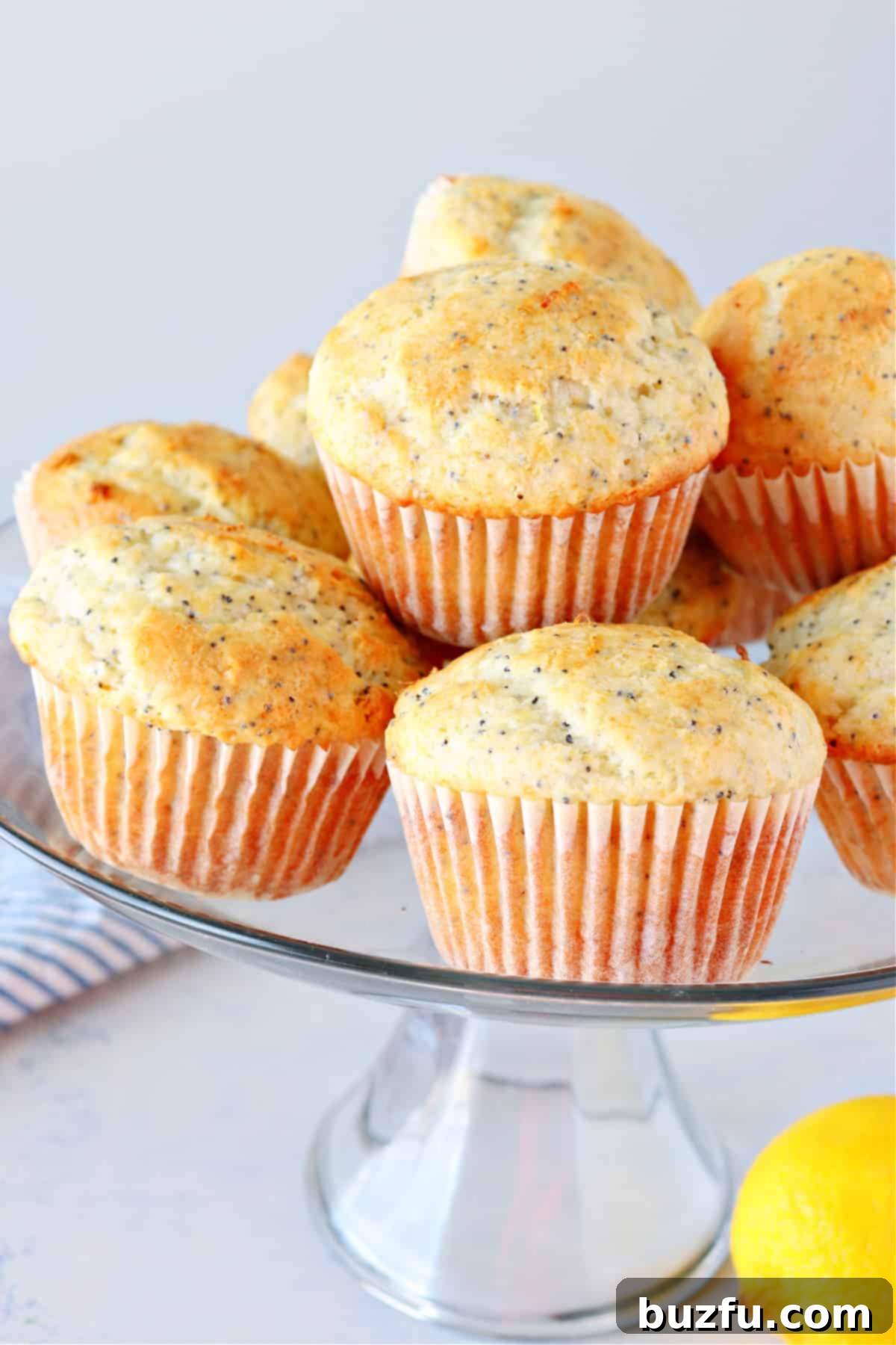 Freshly baked lemon poppy seed muffins on a glass cake stand, ready to be enjoyed.