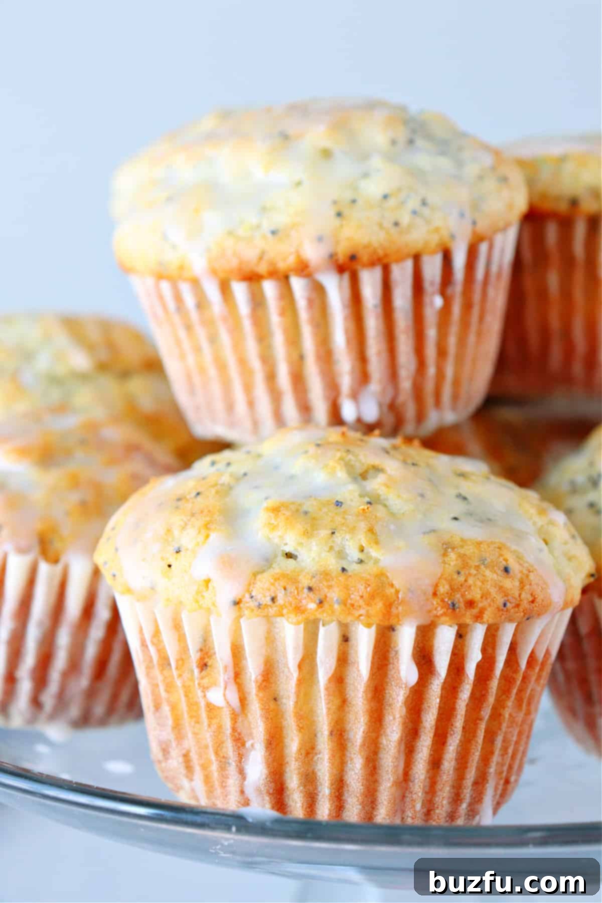 Delicious lemon poppy seed muffins with a sweet lemon glaze on a glass cake stand.