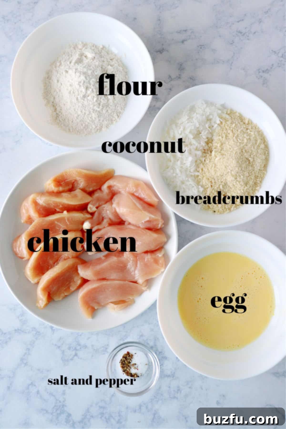 Essential Coconut Chicken Ingredients Fresh ingredients for making coconut chicken laid out on a wooden board, including chicken breasts, flour, eggs, shredded coconut, and panko breadcrumbs.