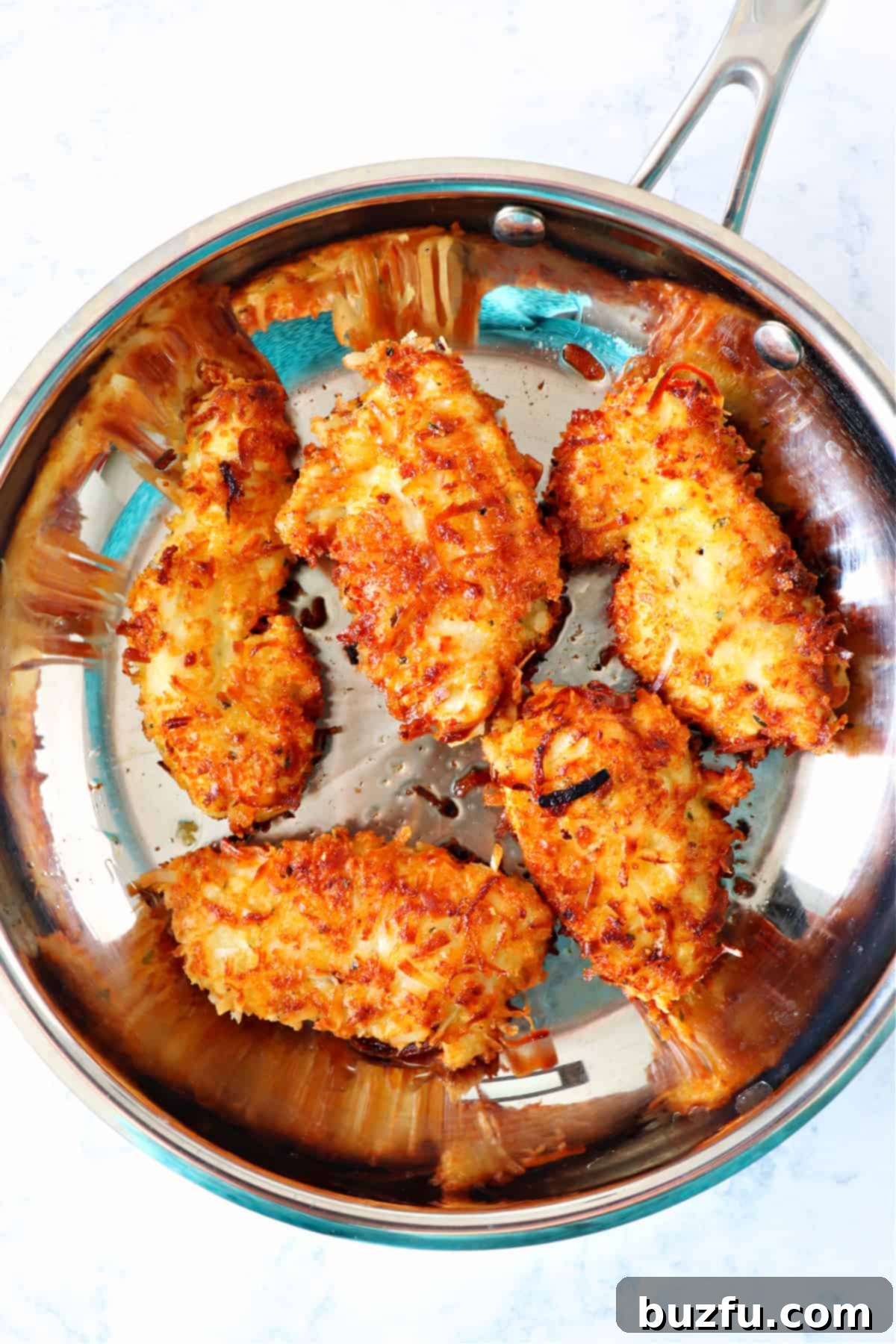 Easy Pan-Fried Coconut Chicken Several pieces of crispy coconut chicken glistening in a hot skillet, fresh from frying.