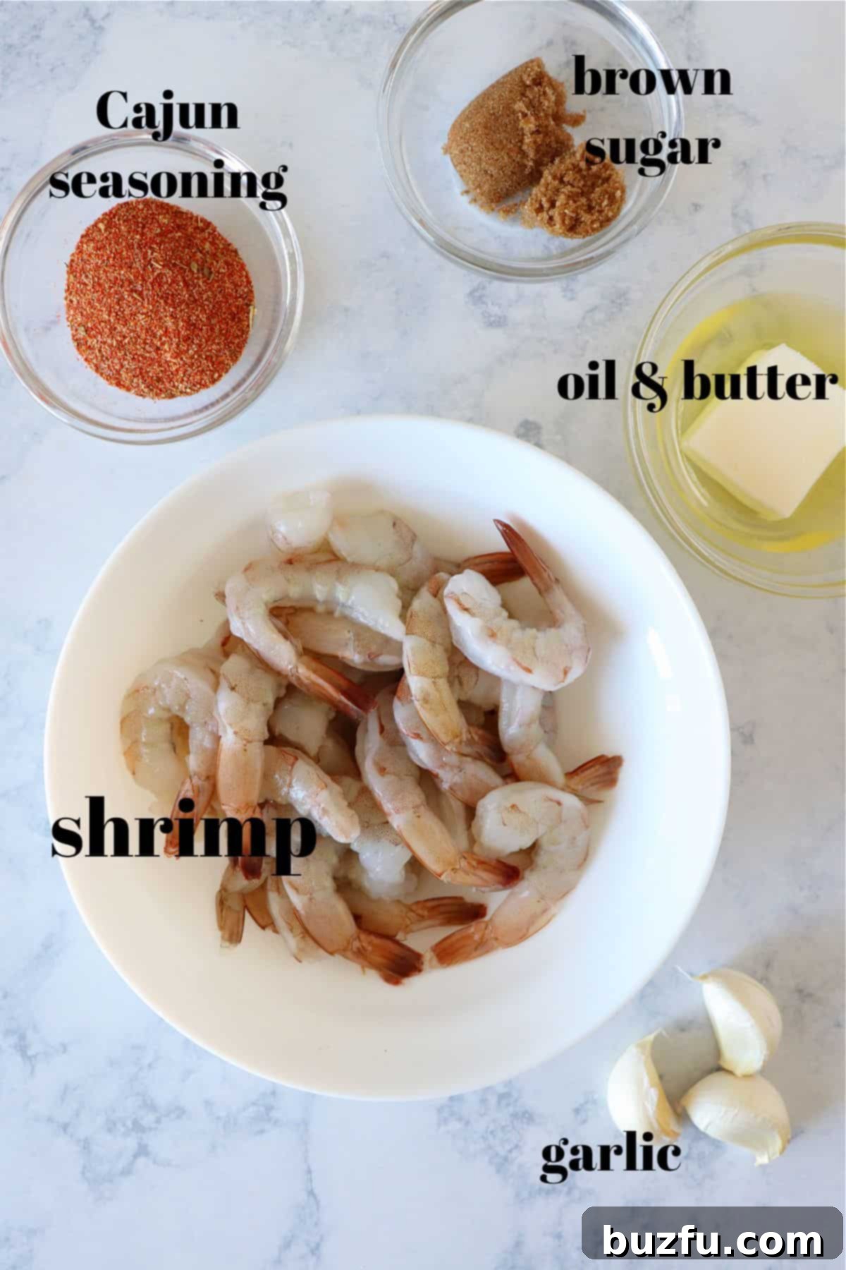 A selection of fresh ingredients laid out on a marble surface, including raw shrimp, garlic, butter, olive oil, and Cajun seasoning, ready for cooking.