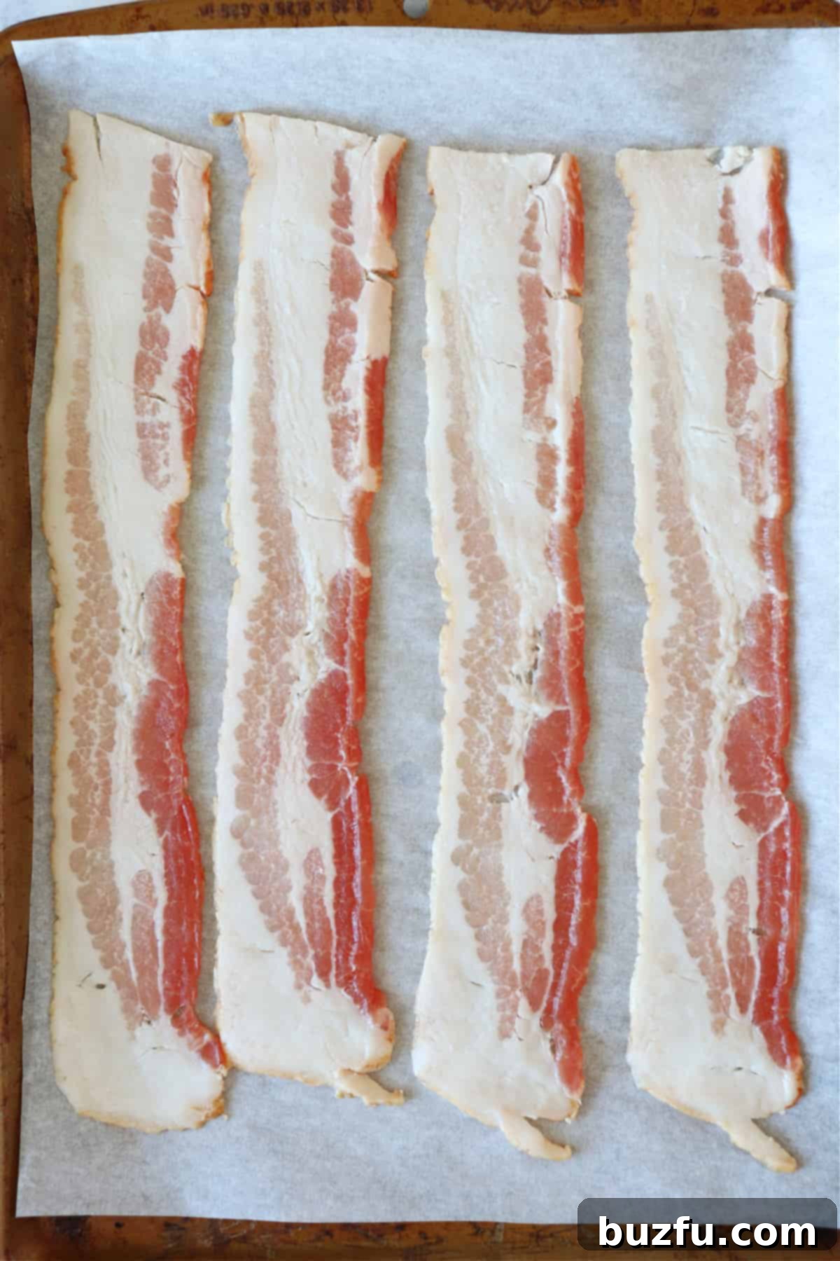 Oven Cooked Bacon recipe Raw bacon strips neatly arranged on a parchment paper-lined baking sheet, ready for the oven.