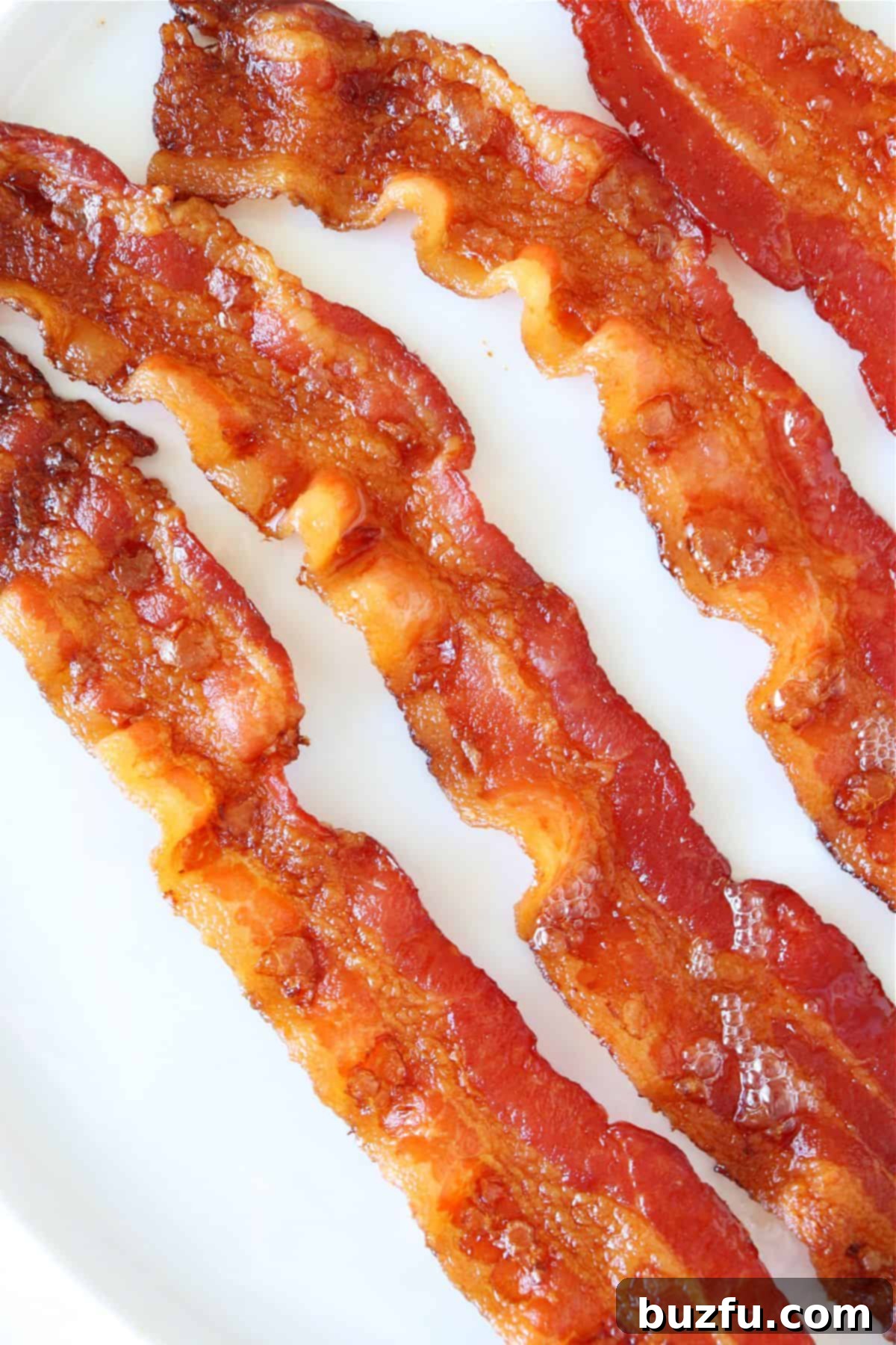 Crispy bacon cooked in the oven. Perfectly cooked, crispy bacon on a white plate, garnished with fresh herbs.