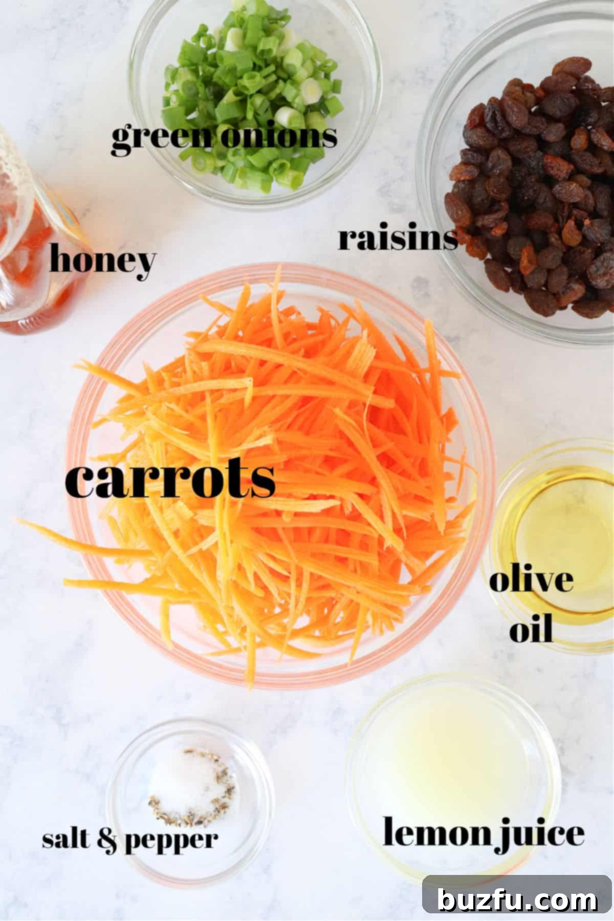Carrot Salad Ingredients Ingredients for carrot salad laid out on a marble board, including fresh carrots, green onions, raisins, olive oil, lemon juice, and honey.