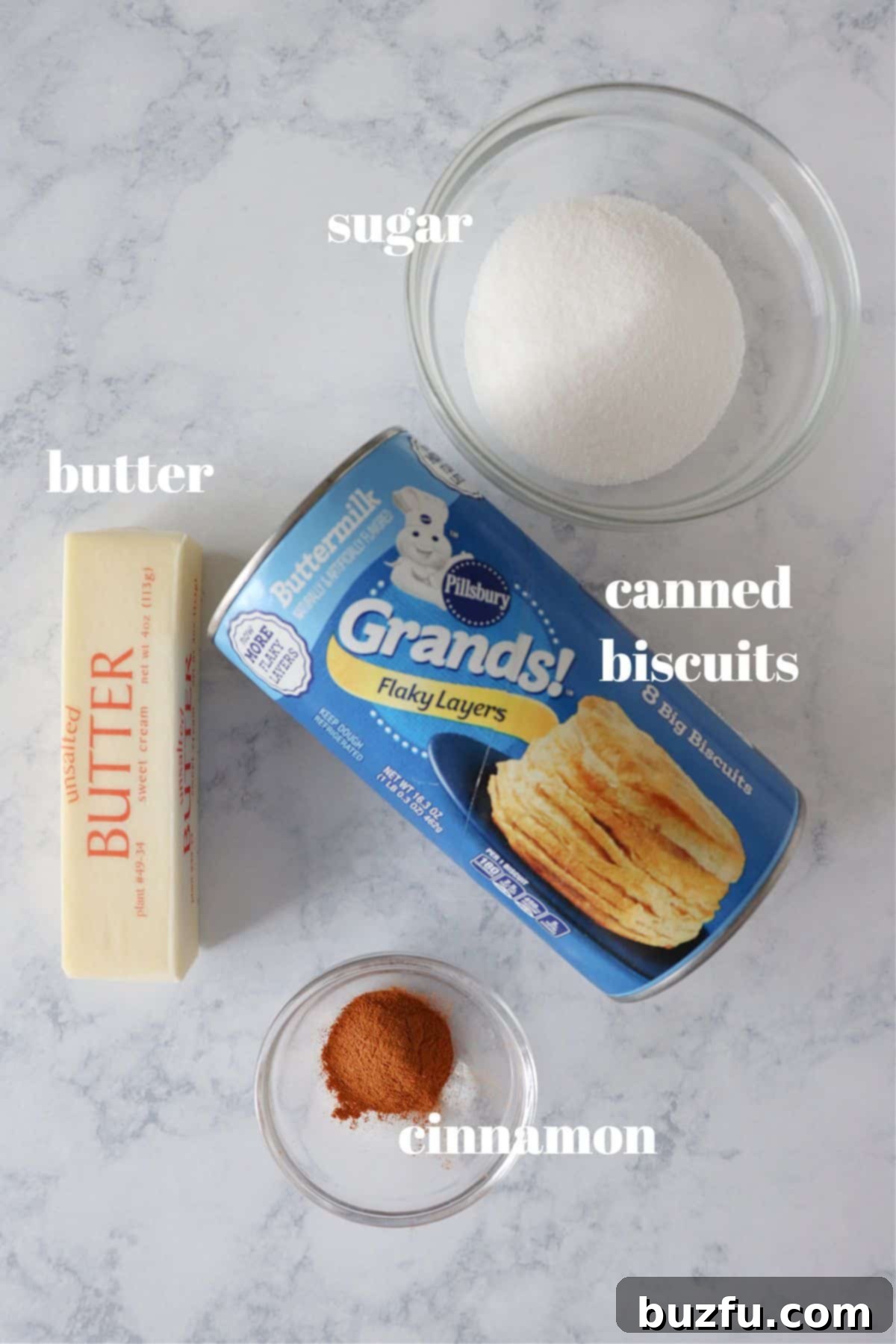 Simple Air Fryer Donut Ingredients List Only a few simple ingredients for air fryer donuts, including a can of biscuits, melted butter, granulated sugar, and ground cinnamon, neatly arranged on a wooden board.