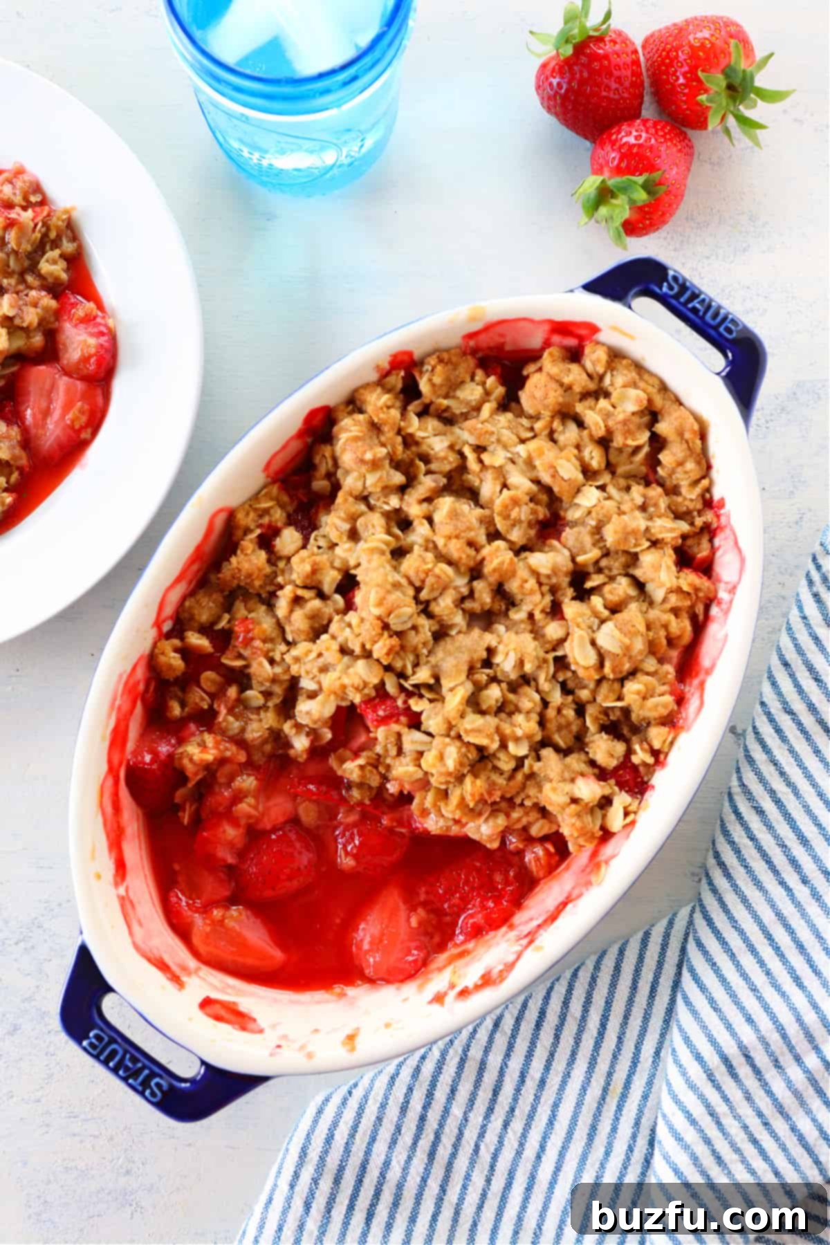 Vibrant strawberry crumble in an oval baking dish, freshly baked with a golden, crispy topping.