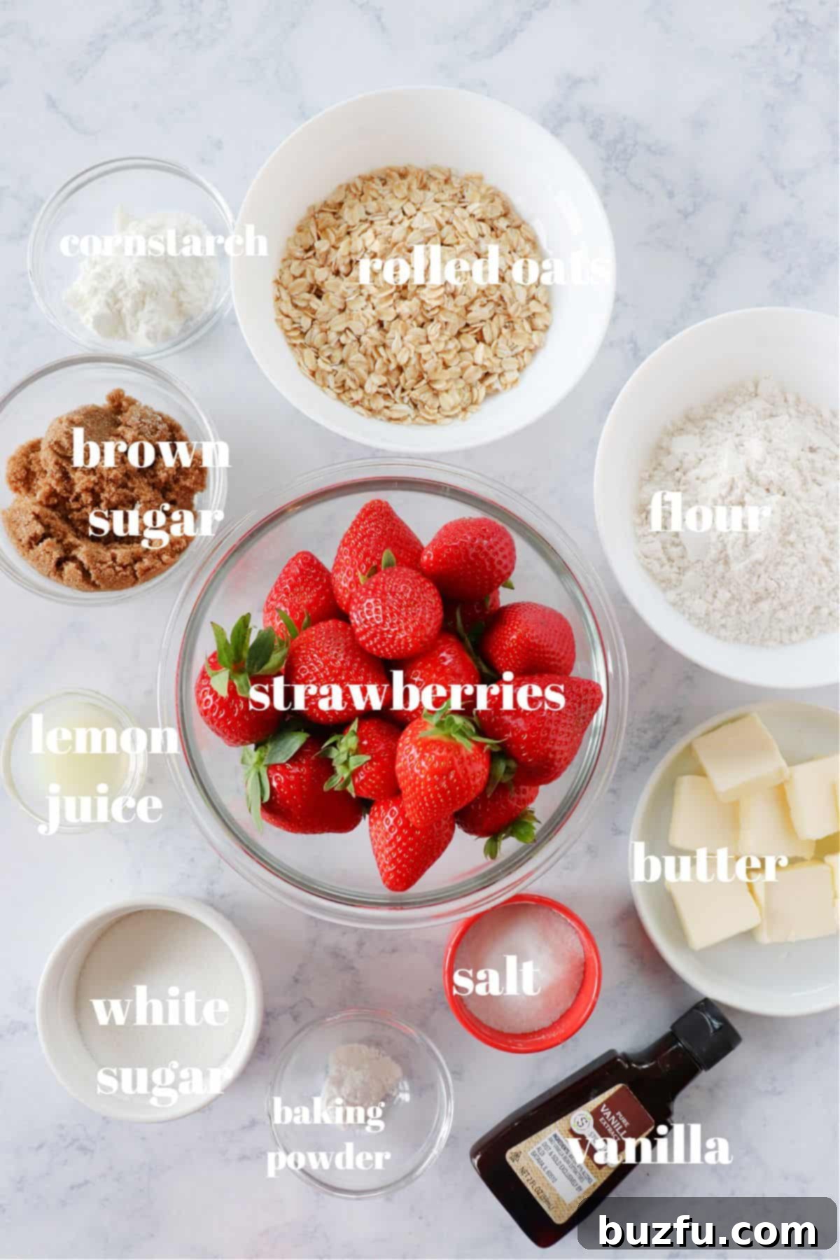 Assorted ingredients for strawberry crumble neatly arranged on a marble board.