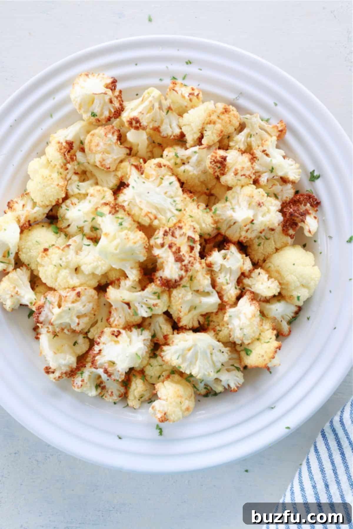 Close-up of golden brown, crispy air fried cauliflower florets on a white plate.