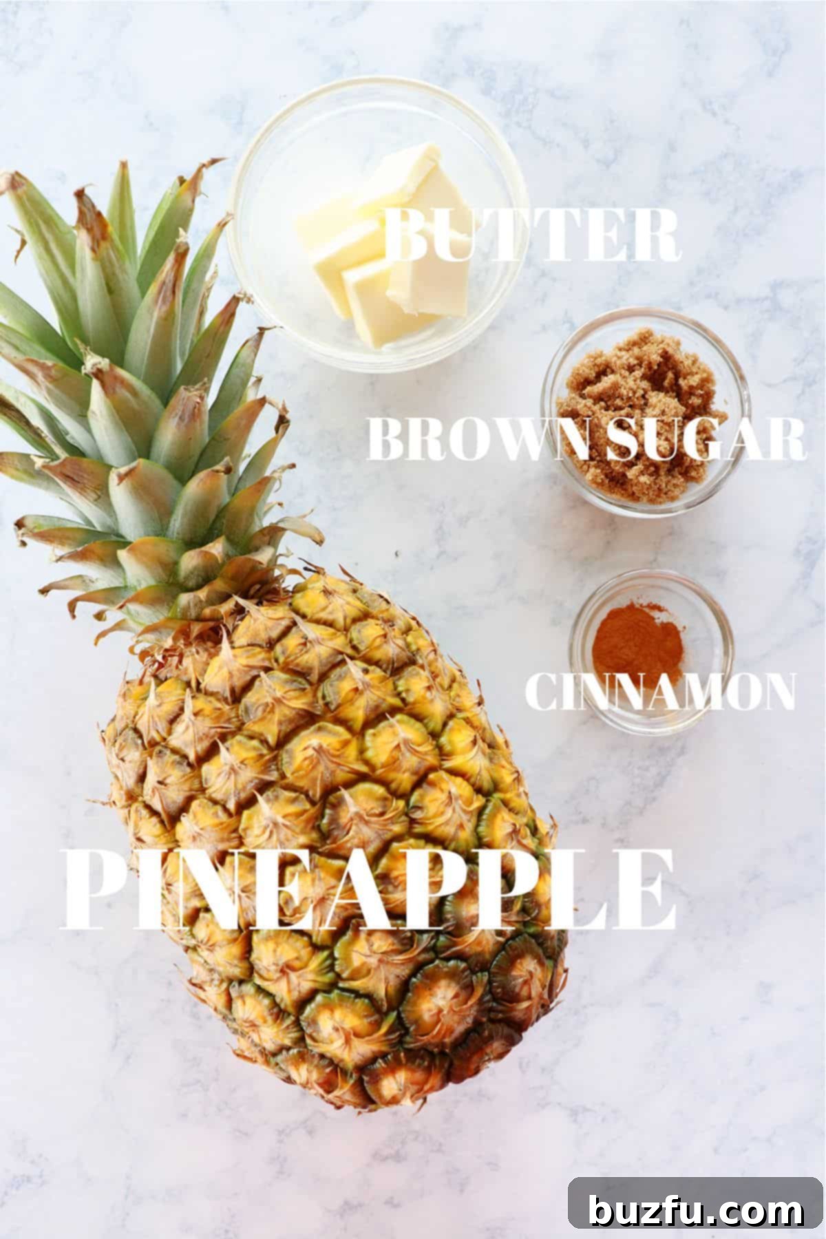 Ingredients for grilled pineapple, including a whole pineapple, butter, brown sugar, and cinnamon, arranged on a marble surface.