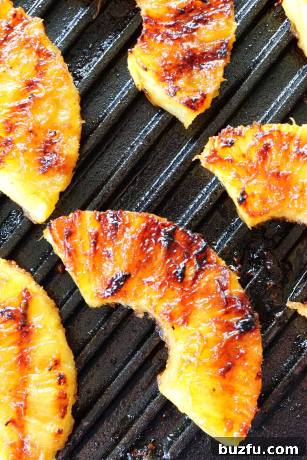 Pineapple slices sizzling on a hot grilling pan, showing developing grill marks.
