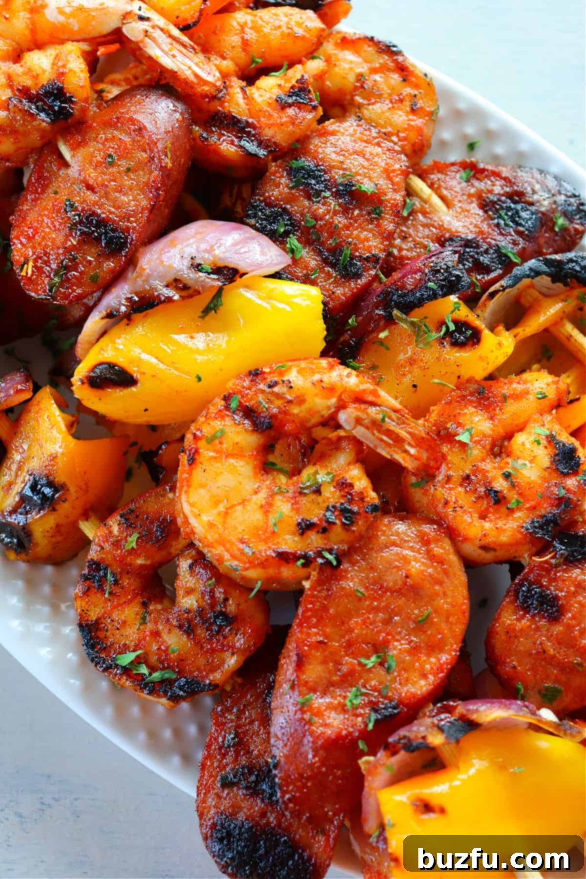 Grilled Shrimp and Sausage Skewers on a white plate, garnished with fresh herbs, ready to be served.