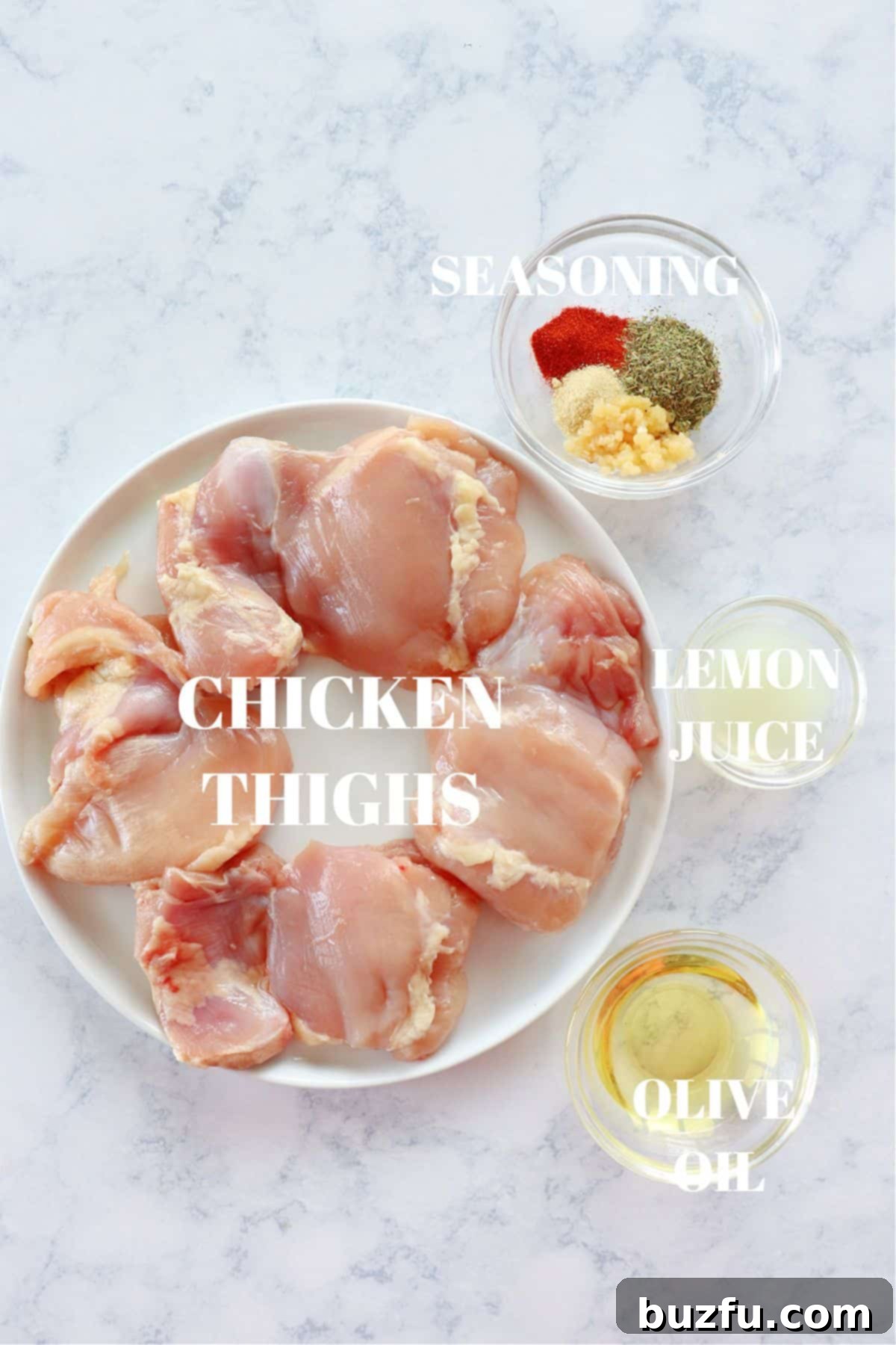 All the fresh ingredients for grilled chicken thighs laid out on a marble board, including chicken, olive oil, lemons, and spices.