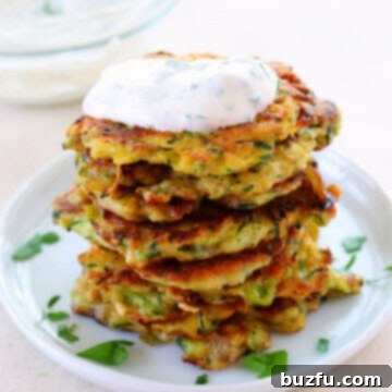 Light and Crispy Zucchini Fritters 2 Stack of zucchini fritters with topping on a plate.