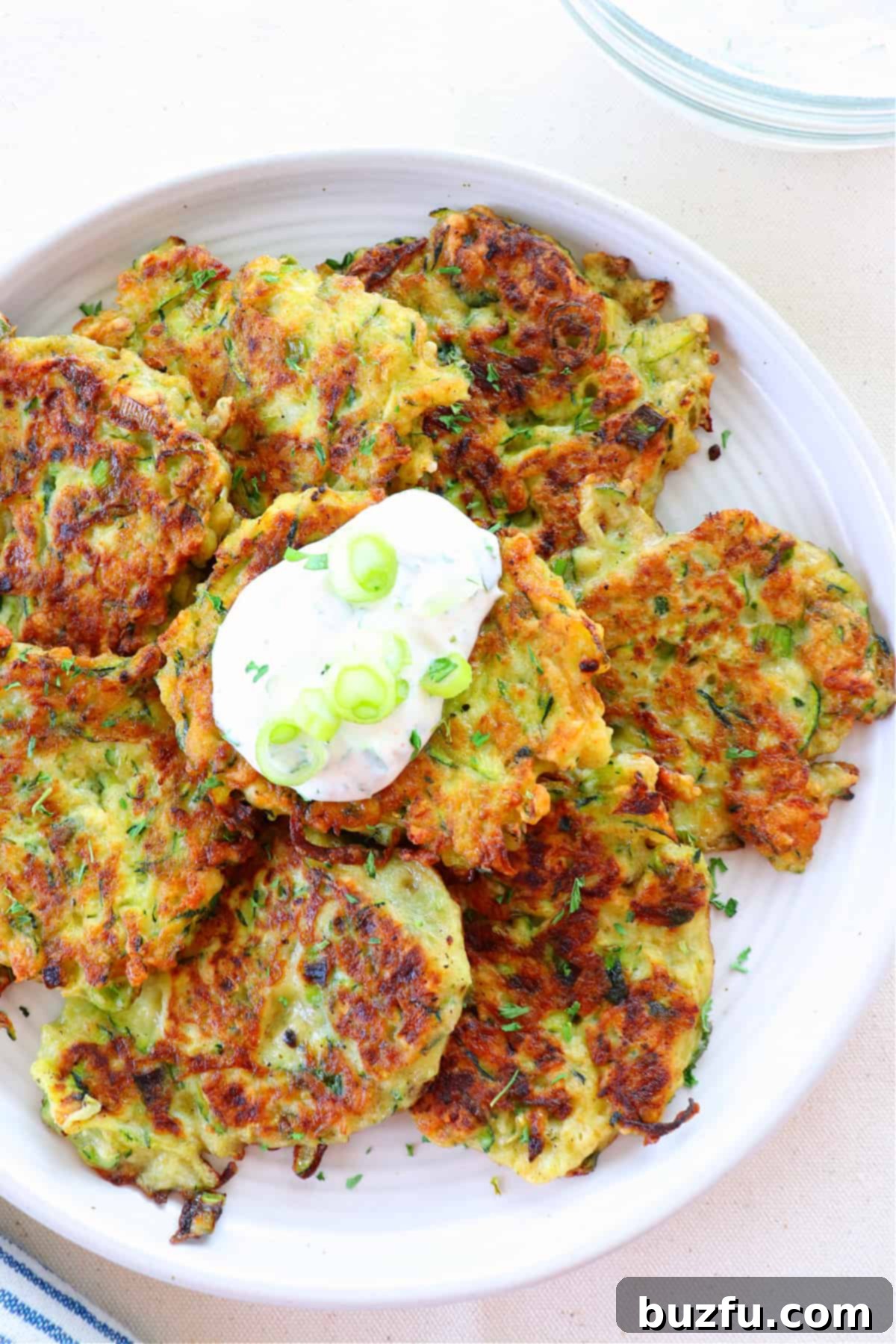 Single Crispy Zucchini Fritter A close-up shot of a single zucchini fritter, perfectly golden and crispy, on a white plate with a fork.
