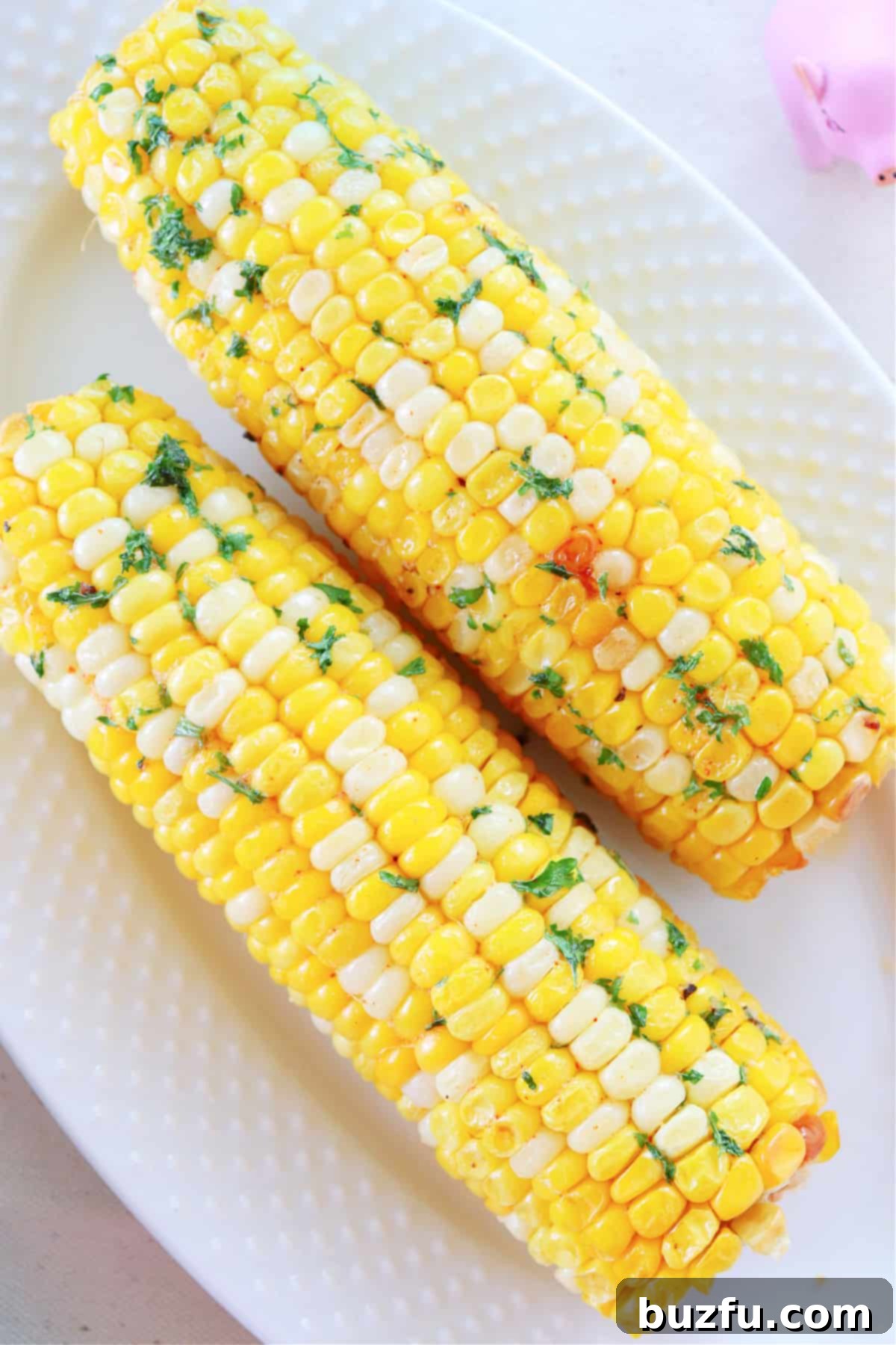 Two cobs of golden-brown air-fried corn on a white plate, ready to be served.