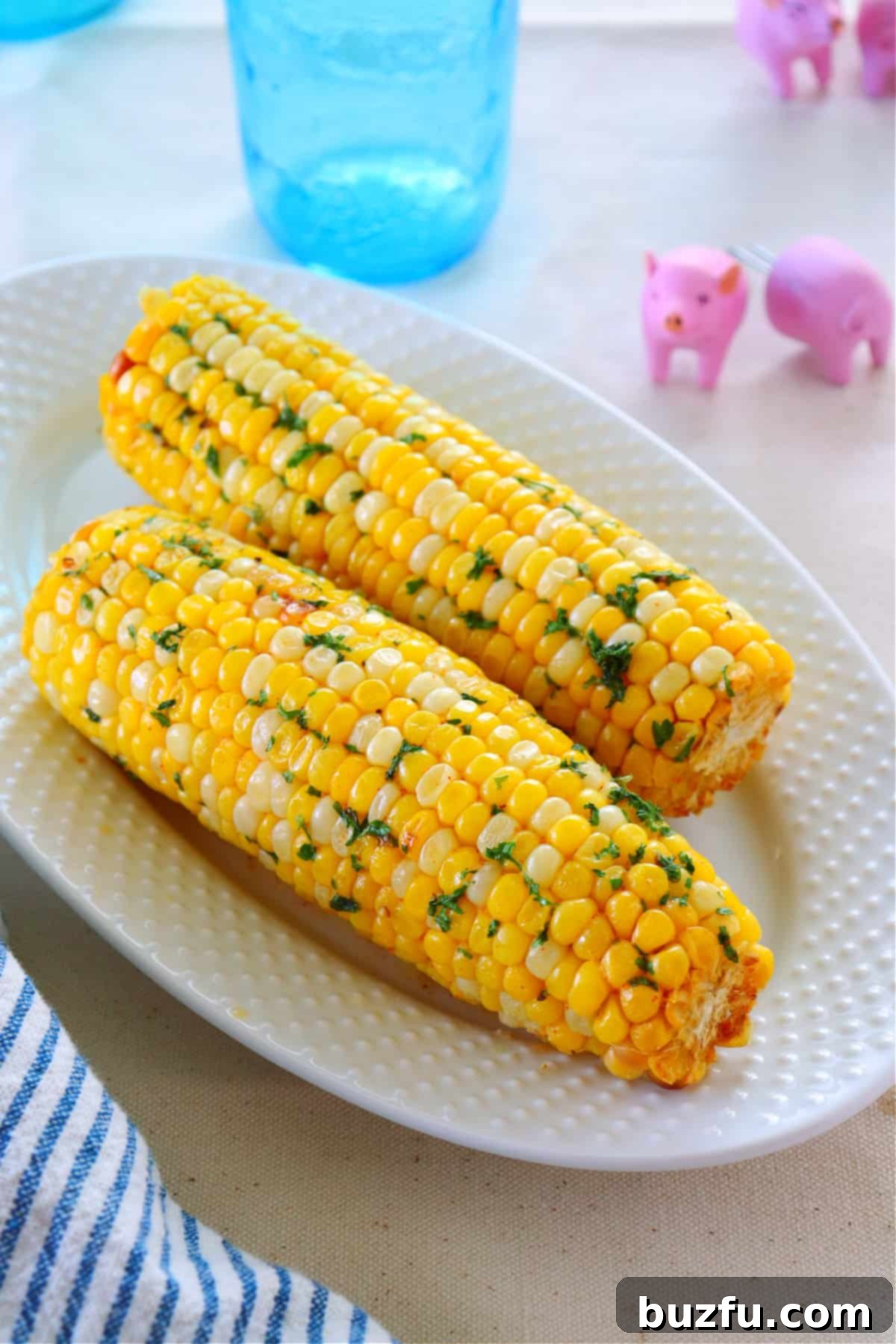 A single cob of perfectly cooked air-fried corn resting on a pristine white plate, garnished with fresh herbs.