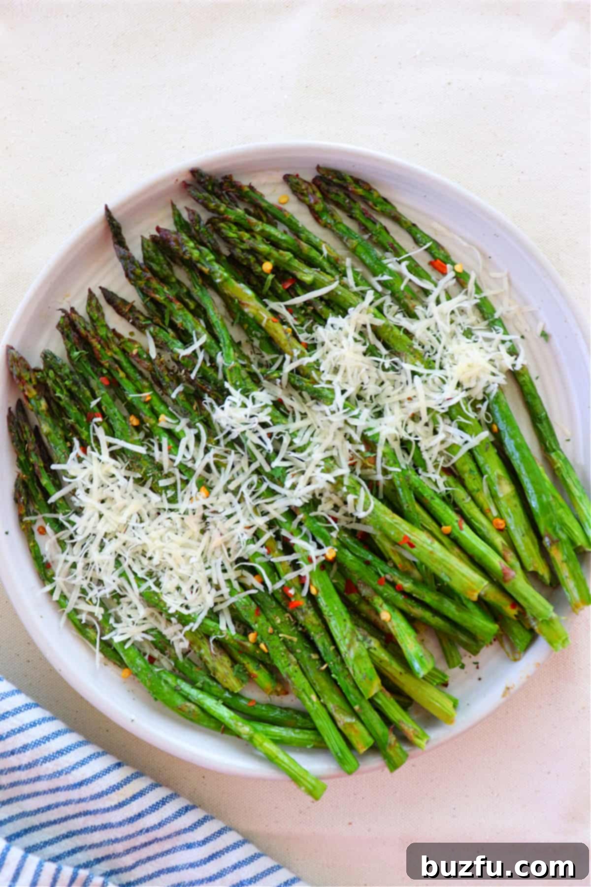 Cooked air-fried asparagus with grated Parmesan cheese and lemon wedges on a white plate.