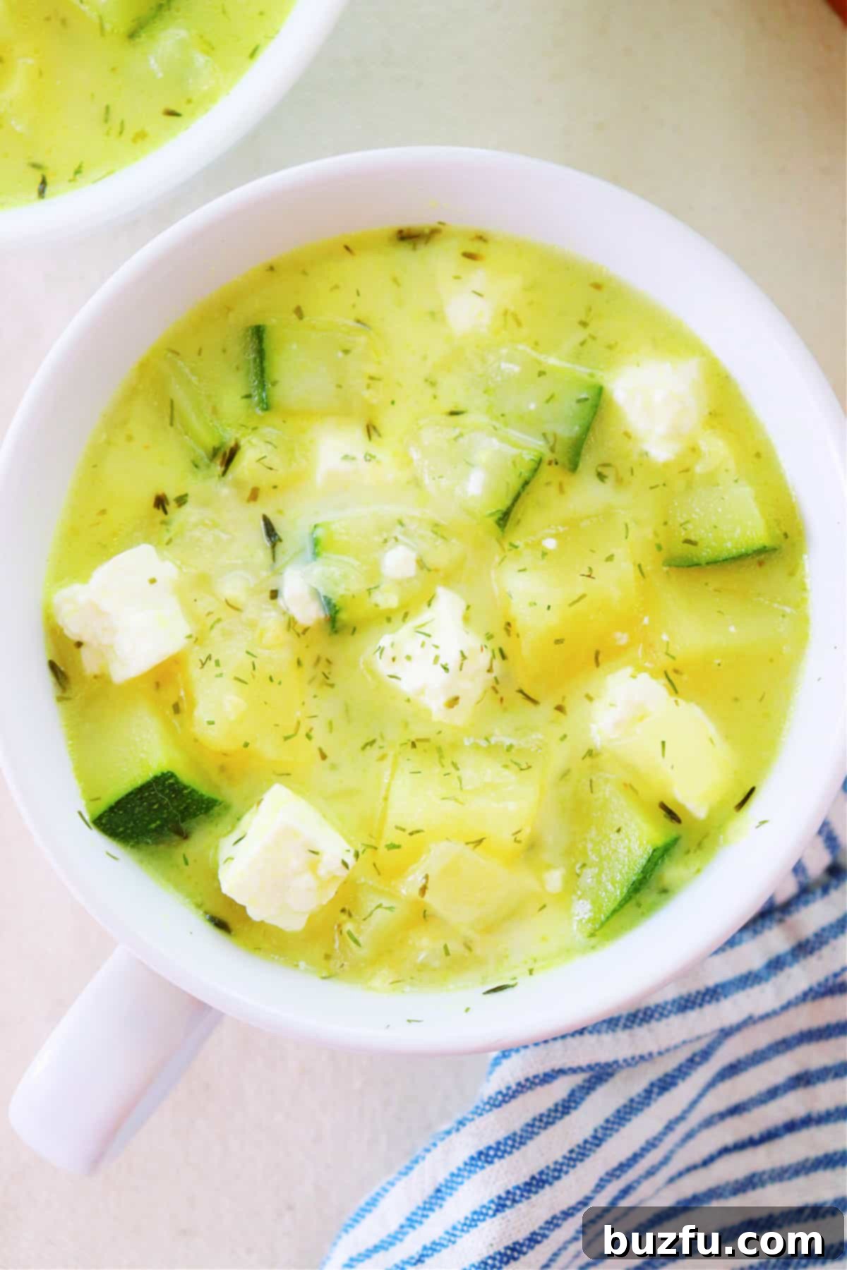 A steaming bowl of creamy zucchini soup garnished with fresh herbs and crumbled feta cheese.