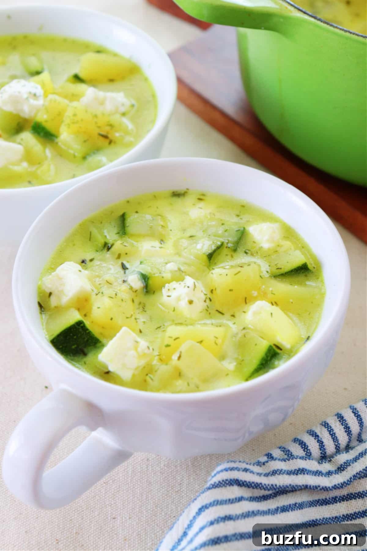 Two bowls of chunky zucchini and potato soup, garnished with fresh dill and crumbled feta, ready to be served.