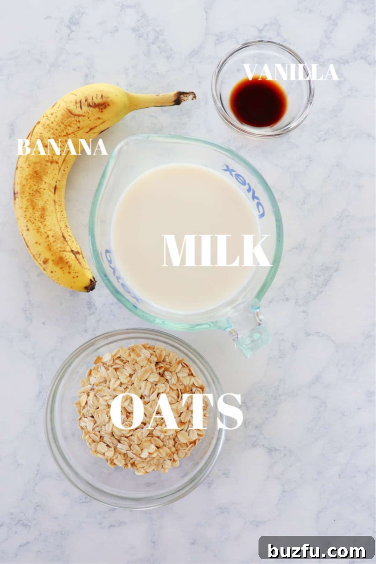 A beautifully arranged spread of fresh and wholesome ingredients including a banana, old-fashioned oats, milk, and vanilla extract on a clean marble surface, ready for blending into a delicious oatmeal smoothie.