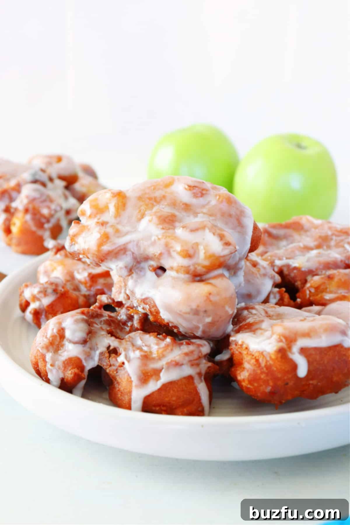 Crispy, glazed apple fritters piled high on a white plate, ready to be enjoyed.