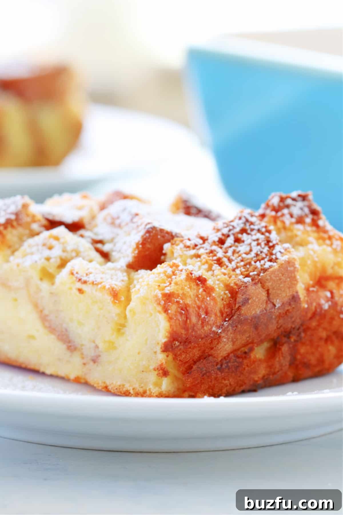 Close-up shot of a slice of bread pudding on a white plate, showing the custardy interior and golden crust.