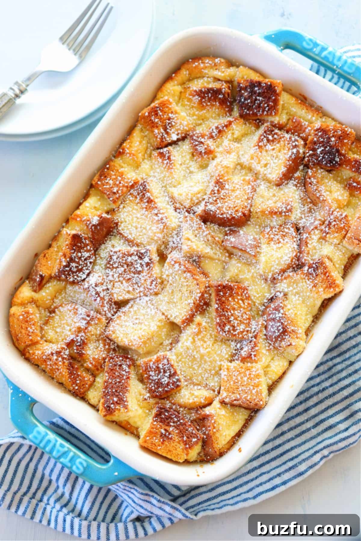 Overhead shot of a baked bread pudding in a blue casserole dish, garnished with powdered sugar.