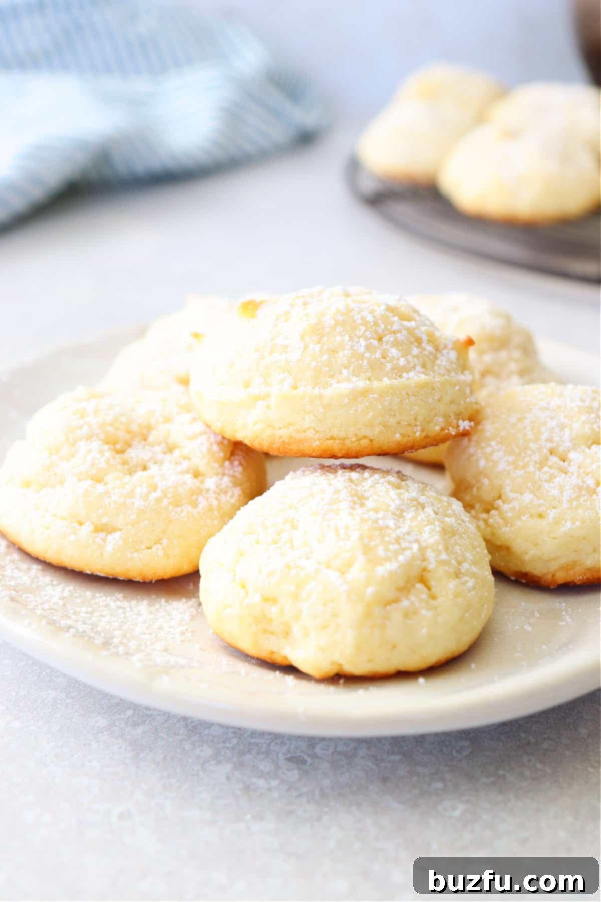Soft and chewy cream cheese cookies dusted with powdered sugar, arranged on a small white plate, ready to be enjoyed.