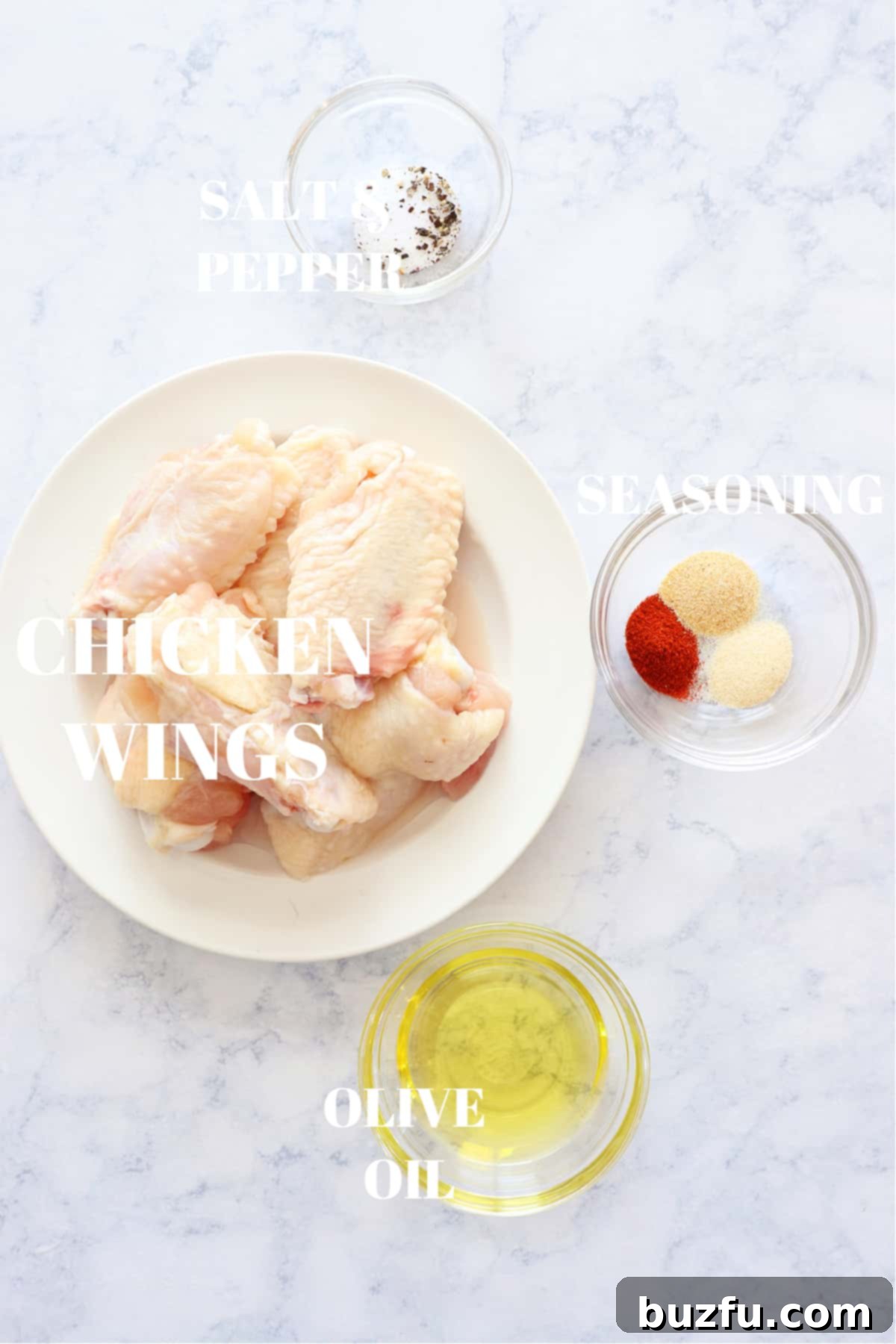 Air Fryer Chicken Wings ingredients A selection of fresh ingredients for air fryer chicken wings including raw chicken wings, olive oil, salt, pepper, garlic powder, onion powder, and paprika laid out on a marble board.