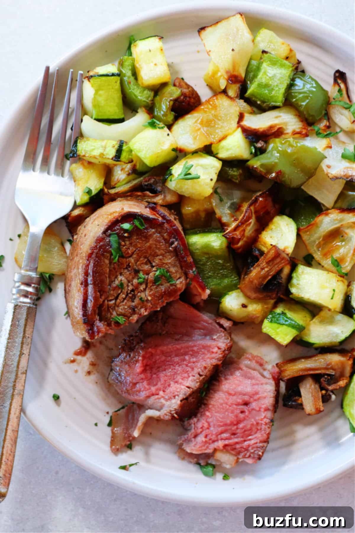 Perfectly cooked, sliced filet mignon with crispy bacon and roasted vegetables on a plate.