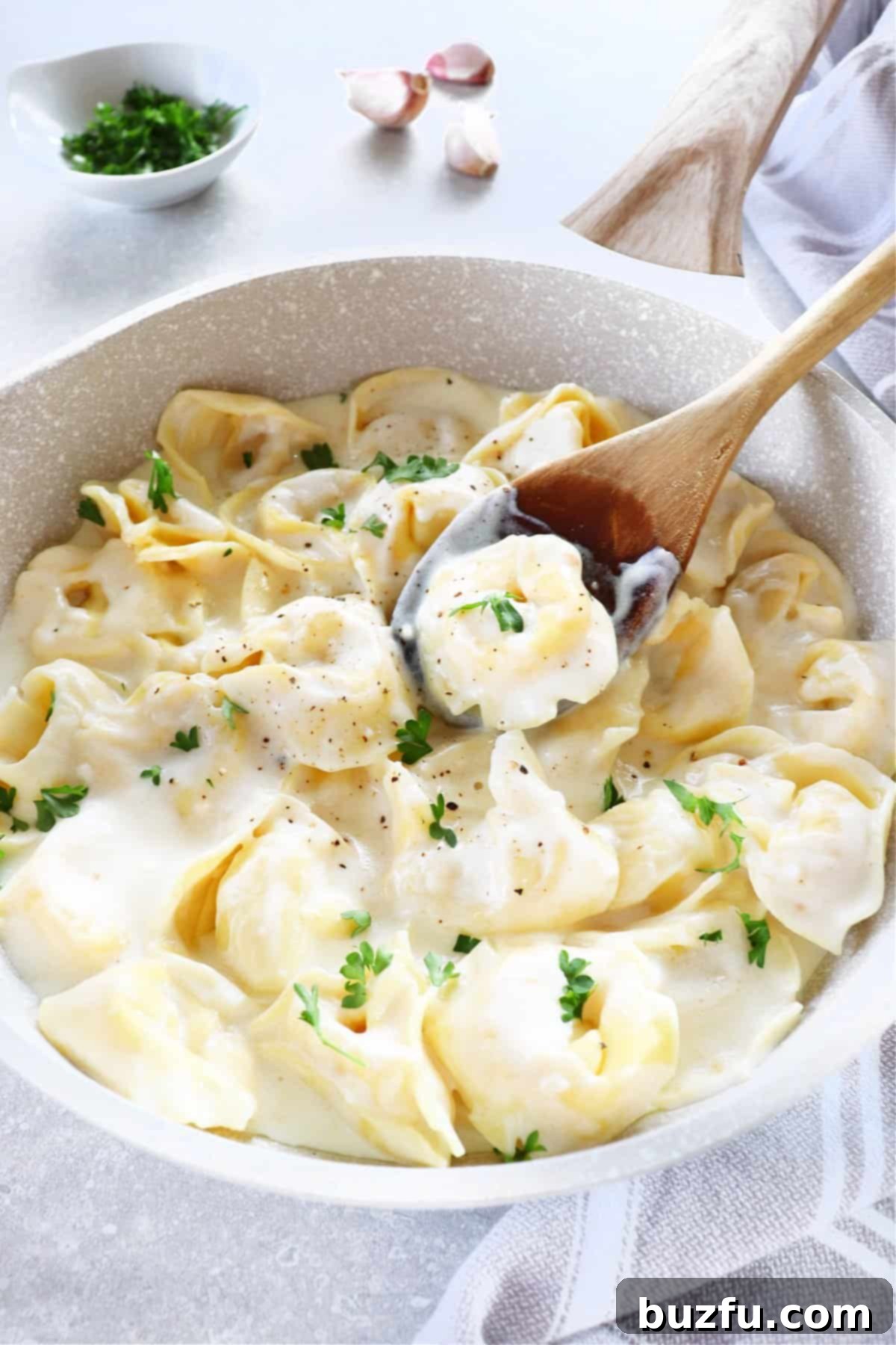 Close-up of creamy Tortellini Alfredo garnished with parsley in a pan.