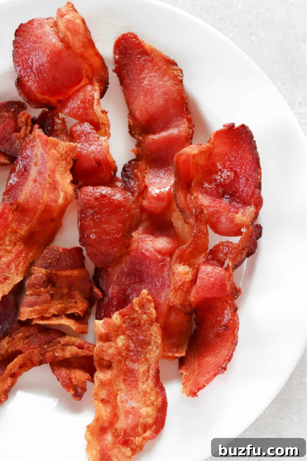 Close-up of perfectly cooked, crispy bacon slices arranged on a clean white plate, highlighting their golden-brown color and inviting texture.
