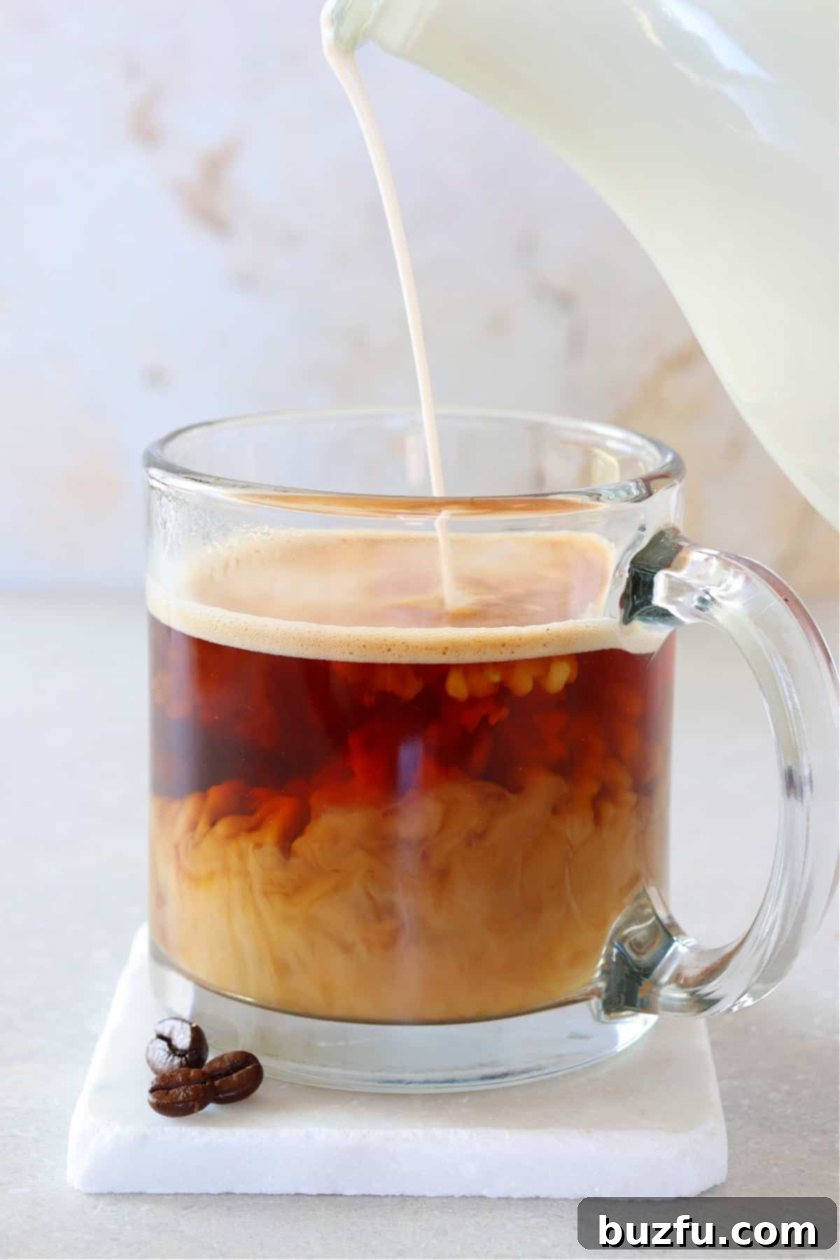 A generous stream of homemade coffee creamer being poured into a mug of freshly brewed coffee, creating a beautiful swirl of light brown and dark coffee.