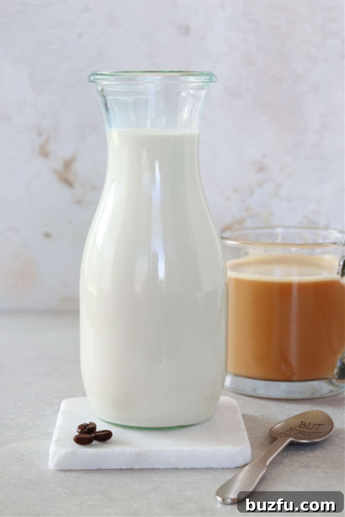 A elegant glass carafe of homemade vanilla coffee creamer sits beside a steaming mug of coffee, ready to be enjoyed.