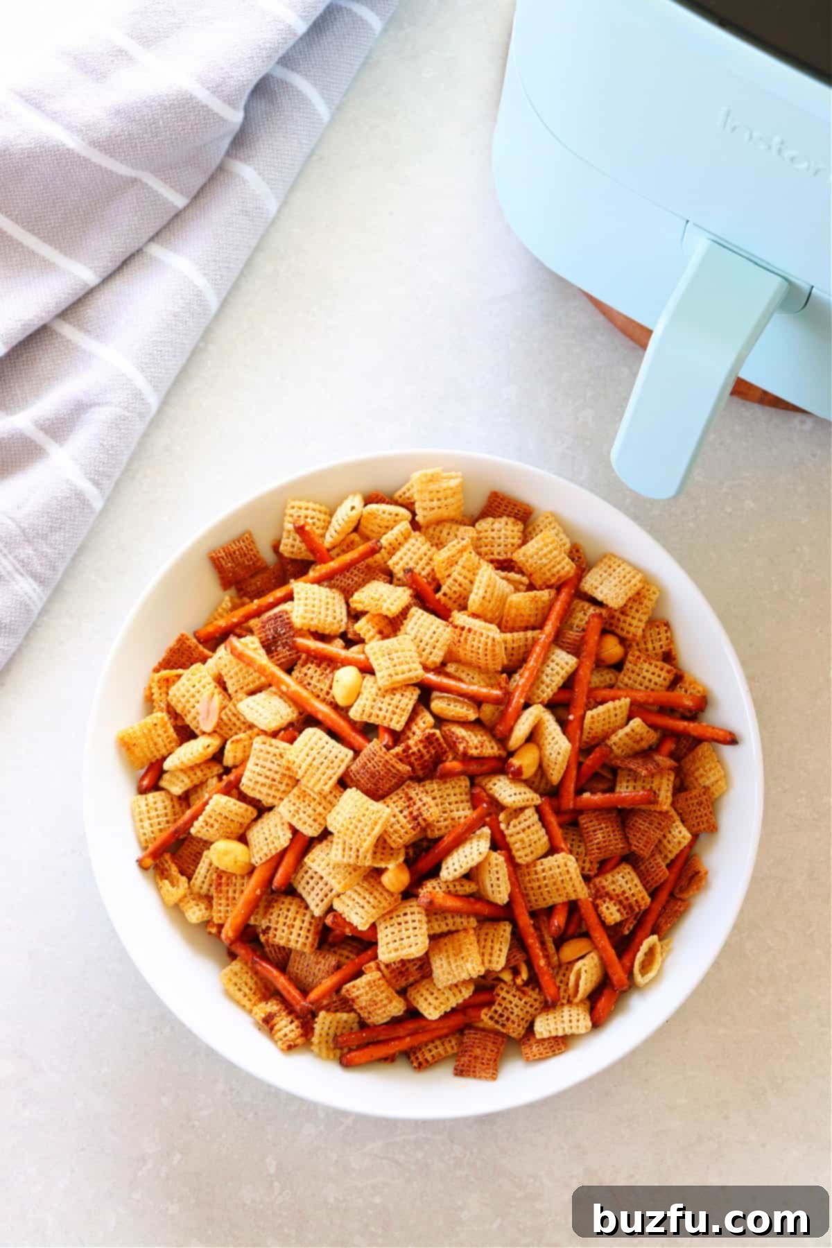 Party mix in white bowl next to air fryer.