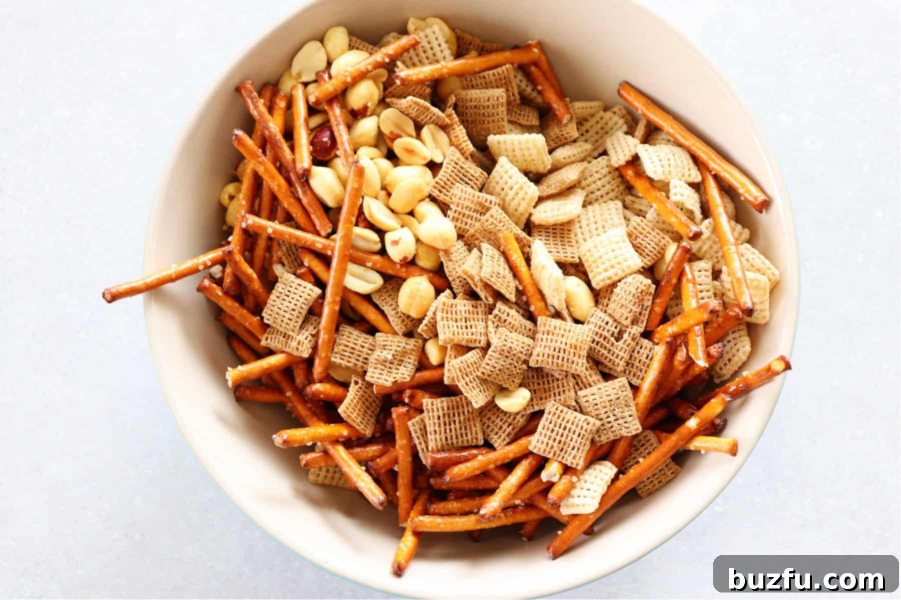 Chex cereal, pretzels and nuts in a bowl.