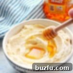 Fluffy whipped butter with a delicate drizzle of honey on a pristine white cutting board.