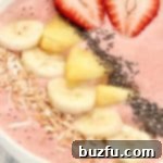 A vibrant strawberry smoothie bowl adorned with fresh pineapple chunks, banana slices, and other colorful toppings.