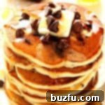 A tall stack of fluffy chocolate chip pancakes on a white plate, ready to be enjoyed for breakfast or brunch.