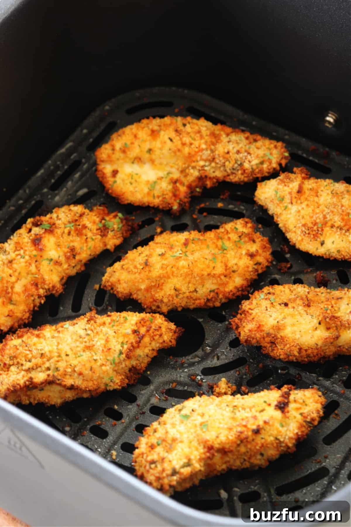 Chicken tenders cooking in an air fryer basket, showing a golden brown, crispy exterior.