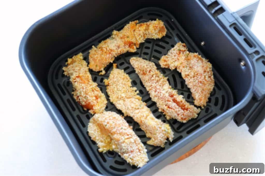 Breaded chicken tenders cooking in an air fryer basket, turning golden brown and crispy.
