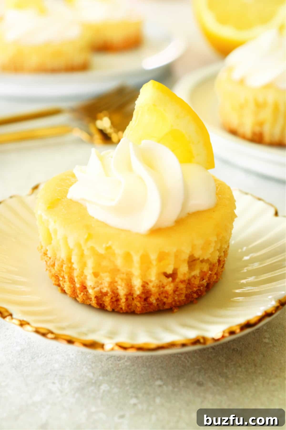 A perfectly portioned mini lemon cheesecake resting on a elegant white plate with a subtle gold rim, highlighting its delicate topping and golden-brown crust.